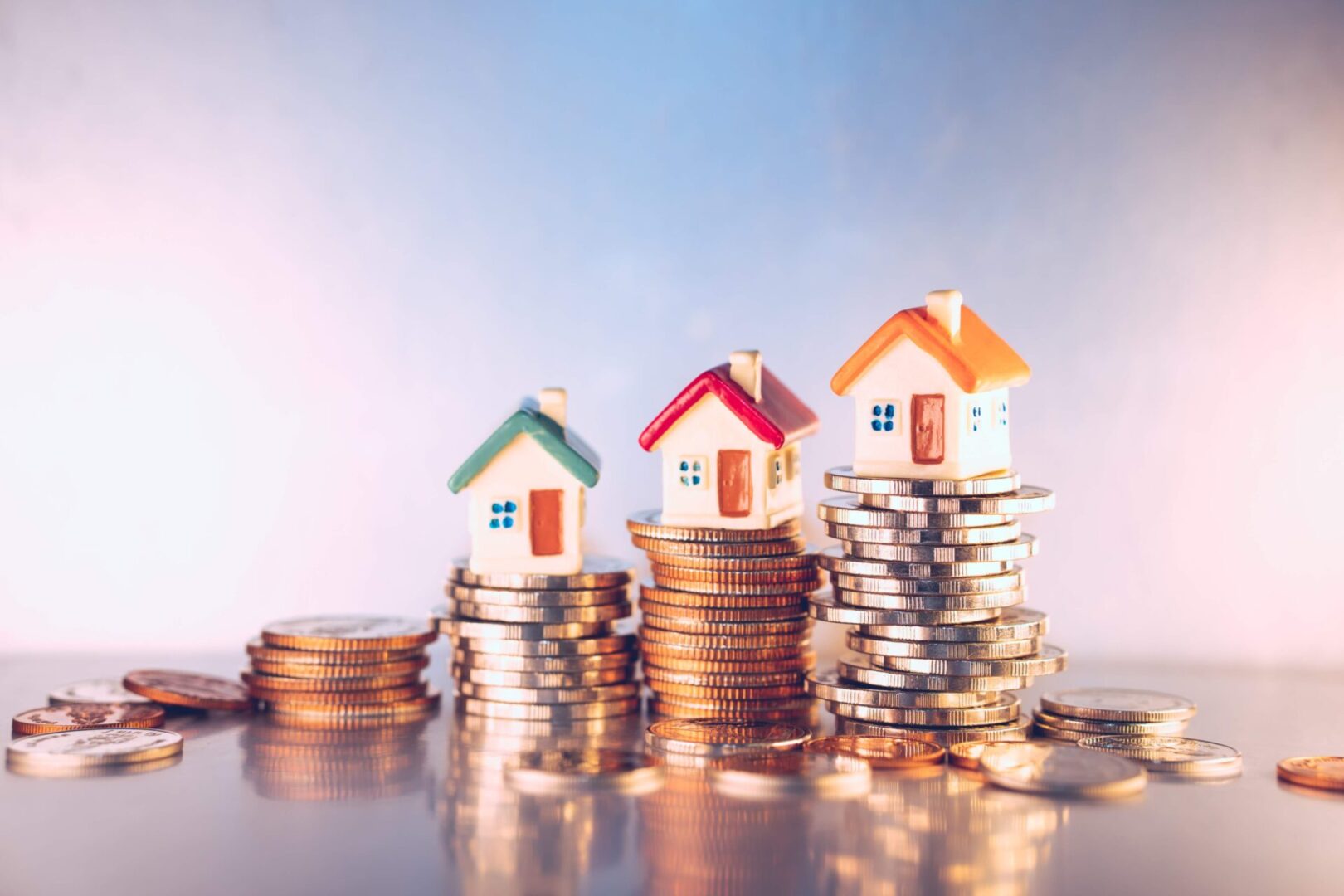 Three small house models on stacks of coins symbolizing real estate investment.